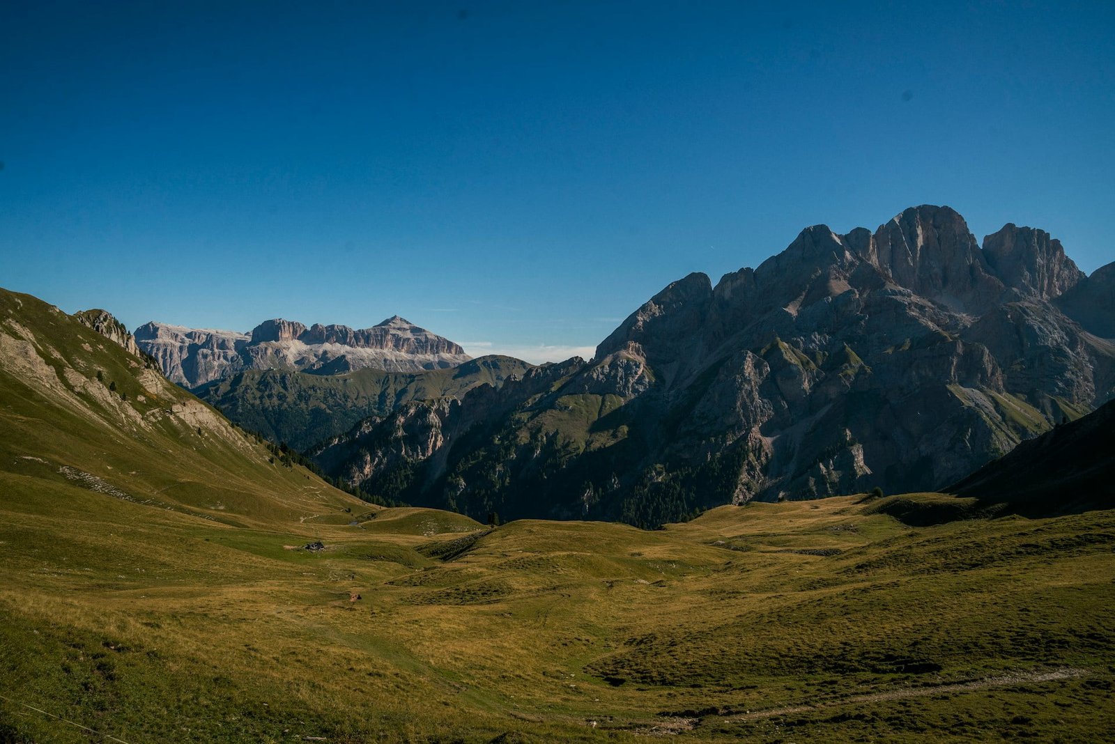 A wide view of a mountainous landscape with rugged peaks and green valleys under a clear blue sky.