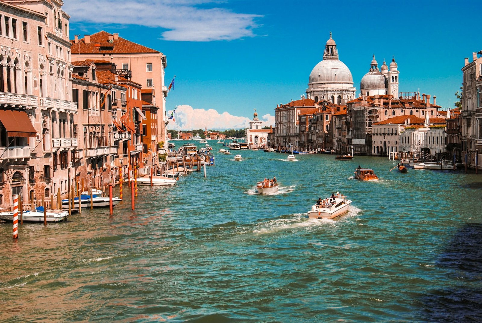 View of Venice's Grand Canal with several boats navigating the waterway, historic buildings lining the sides, and the dome of Santa Maria della Salute in the background under a clear blue sky—truly capturing the best of Italy in 7 days.