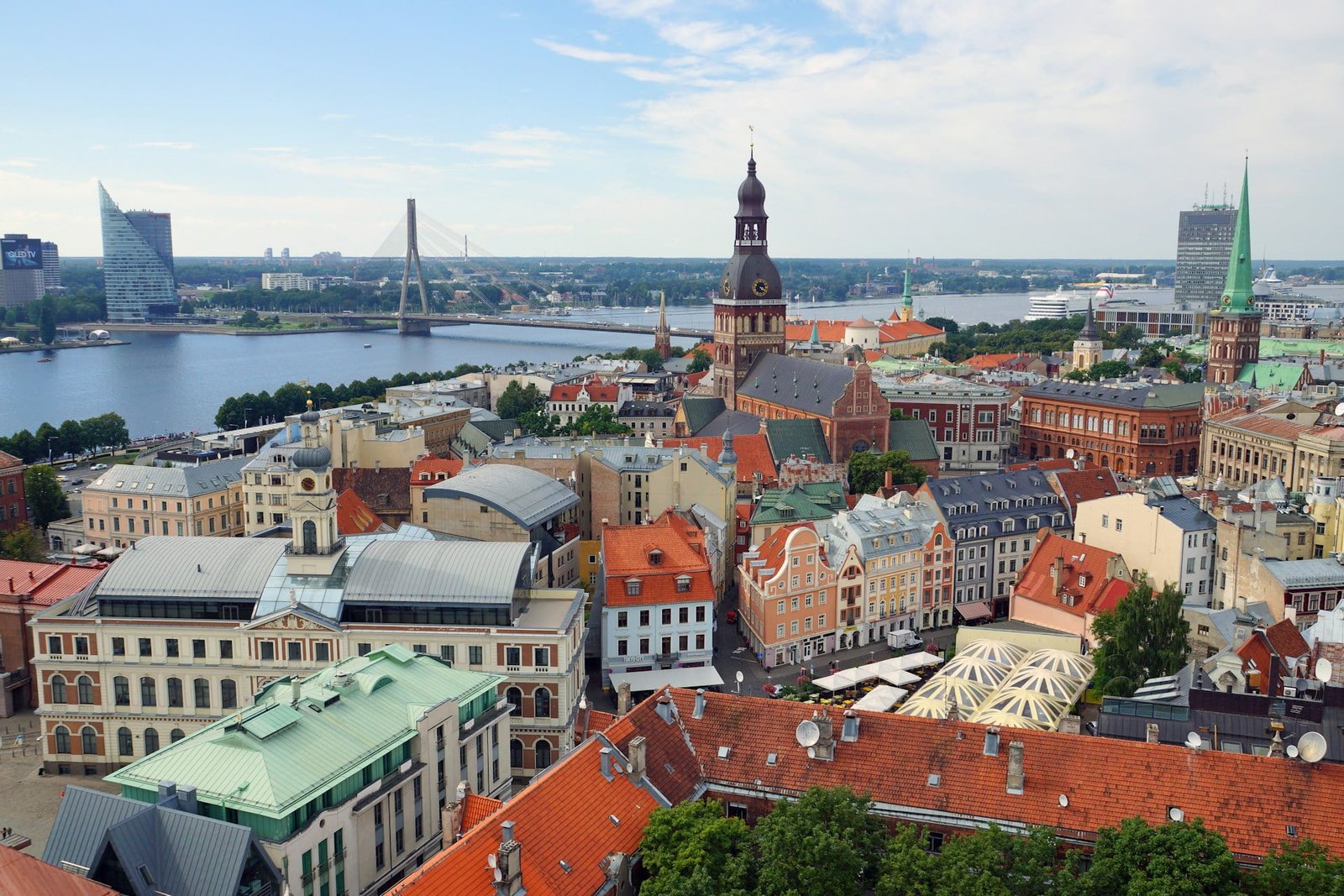 Aerial view of an underrated European destination showcasing a historic city with a mix of modern and old buildings, a church with a tall spire, and a river with bridges in the background under a partly cloudy sky.