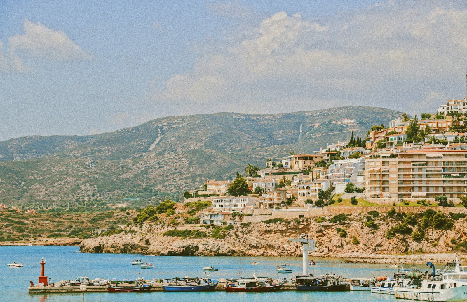 A beautiful coastal view with boats docked by the shore and a hillside town—possibly one of the best vegan spots—with an ocean view.