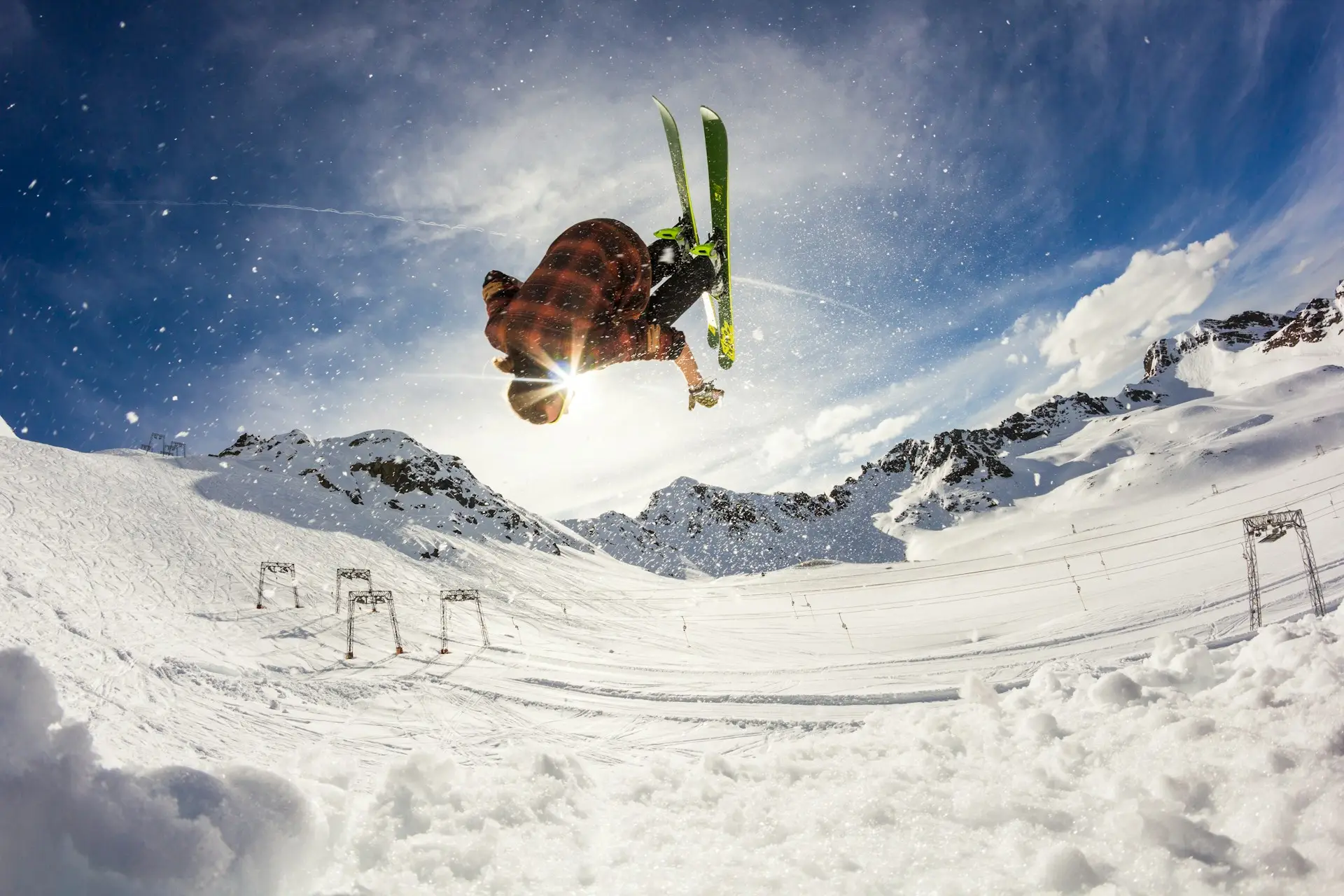 A skier doing a flip in the air with snowy mountains and ski lifts in the background at one of the winter sports destinations in Europe