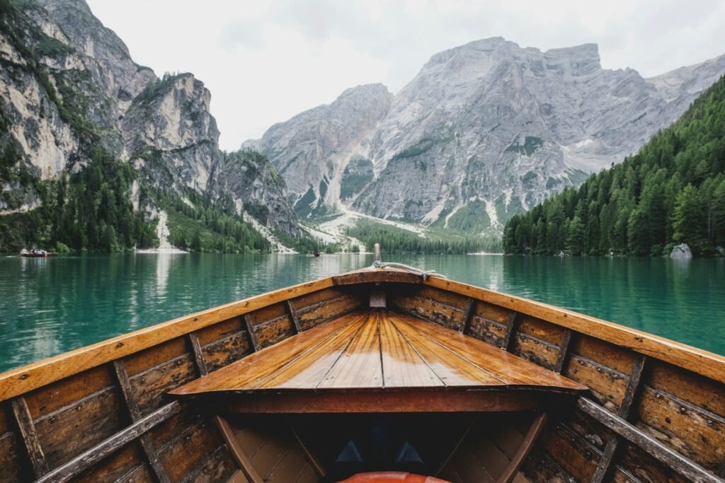 A wooden boat with a pointed bow floats on a clear, serene lake surrounded by majestic mountains and lush greenery, capturing the essence of vegan travel in Europe with its natural and unspoiled beauty.