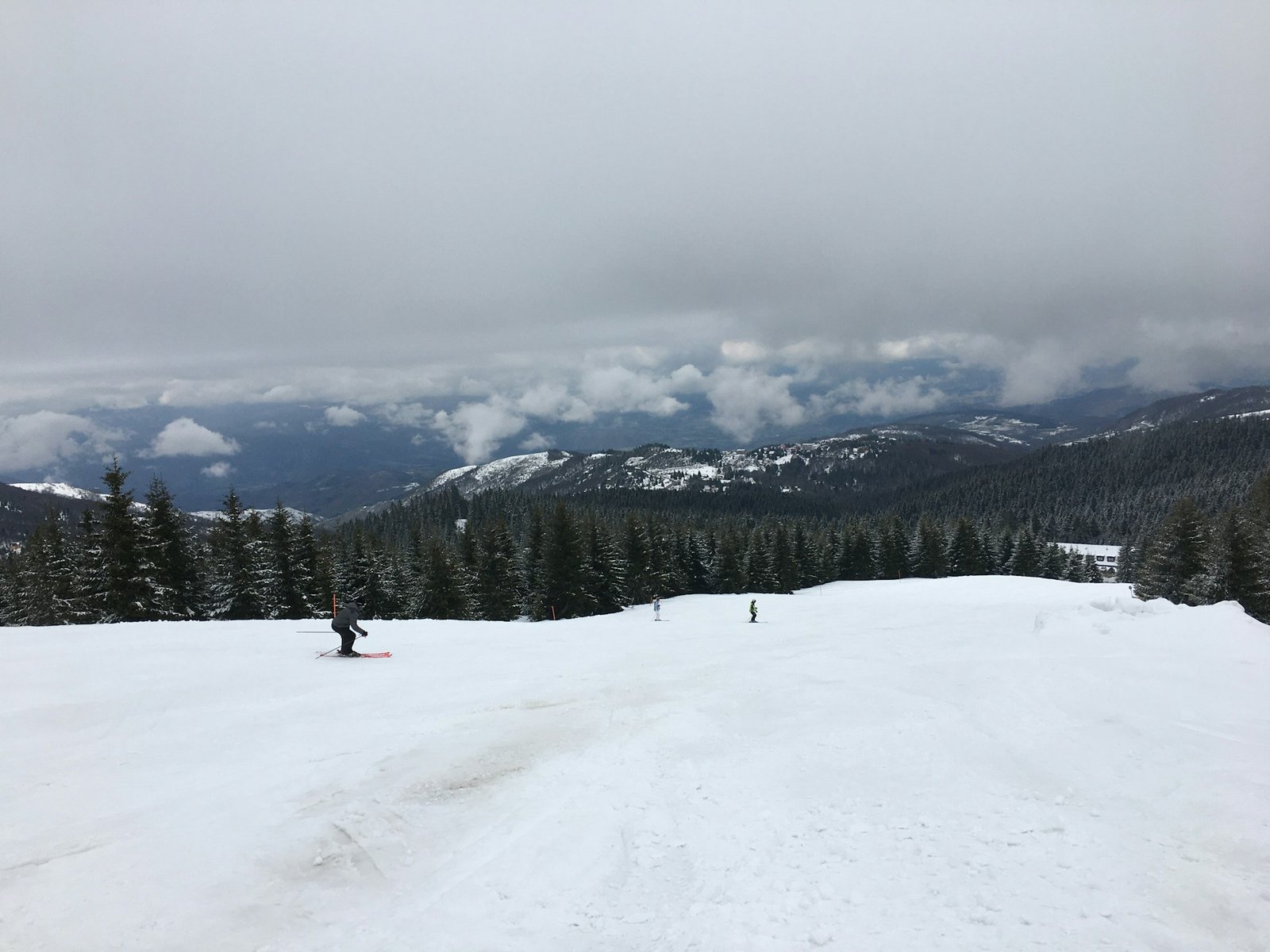 Winter sports destinations in Europe A snowy mountain slope at one of the winter sports destinations in Europe, with people skiing and snowboarding. Pine forests and mountains are in the background under a cloudy sky.
