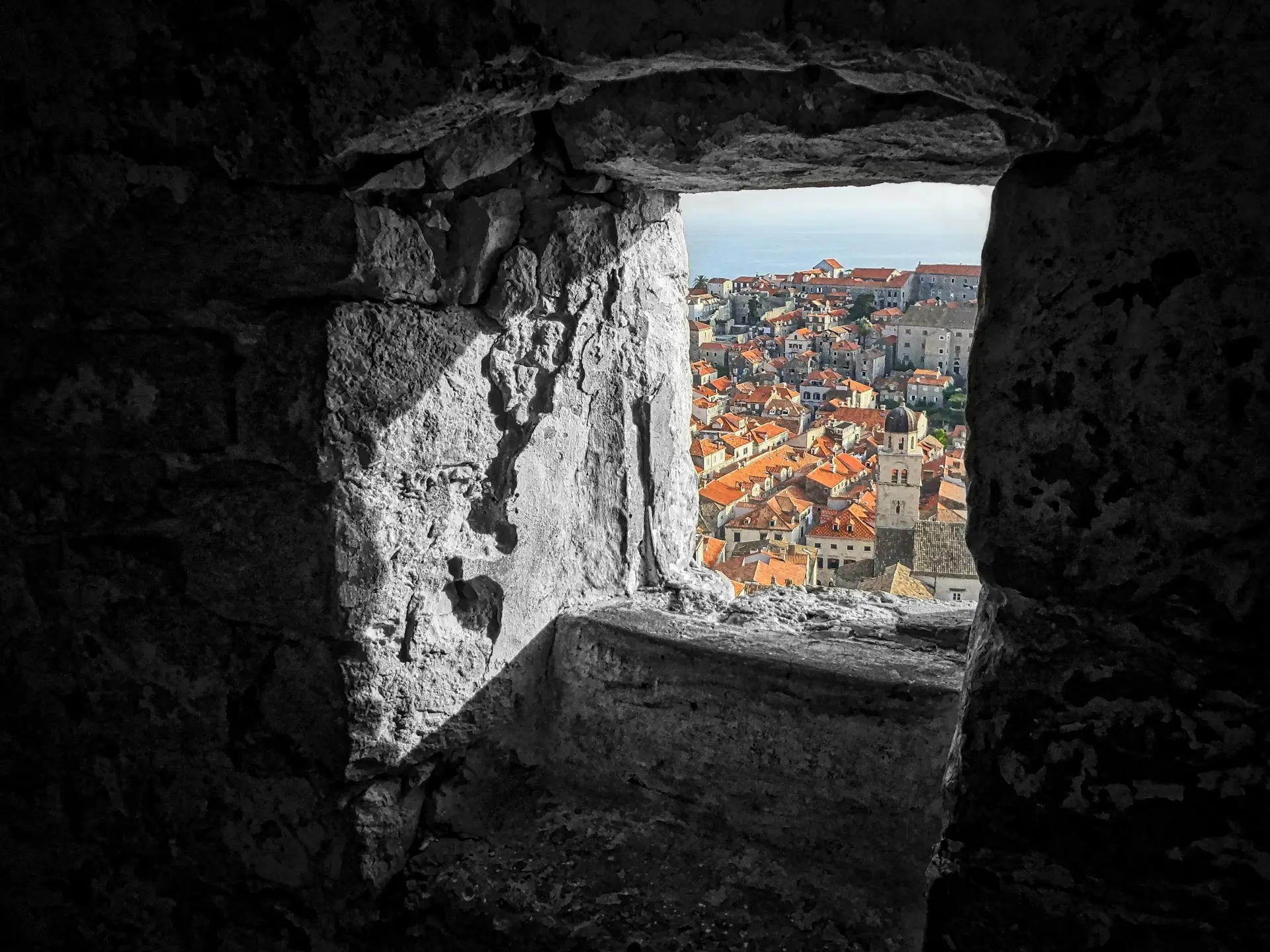 View of Dubrovnik, Croatia through a stone window, showcasing the dense terracotta rooftops and historic architecture, inviting vegan travelers to explore its charm without compromising their lifestyle.