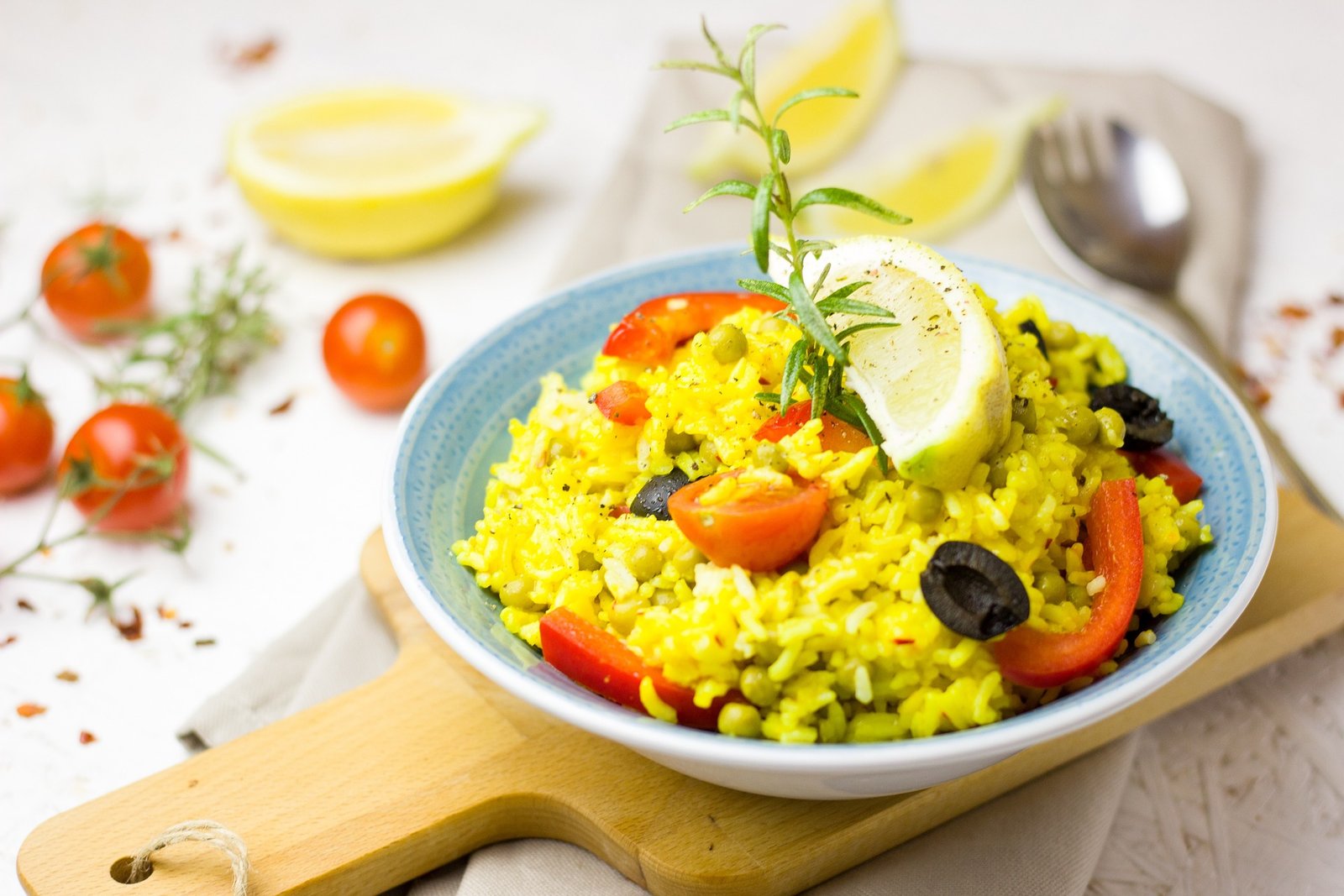 A vibrant vegan paella, a staple of Spanish cuisine, presented in a blue bowl garnished with a lemon wedge and fresh herbs, symbolizing the diverse options available for vegan travel in Europe. The dish features an array of colorful vegetables like tomatoes and bell peppers mixed with rice, showcasing the possibility of enjoying traditional flavors while adhering to a plant-based diet.