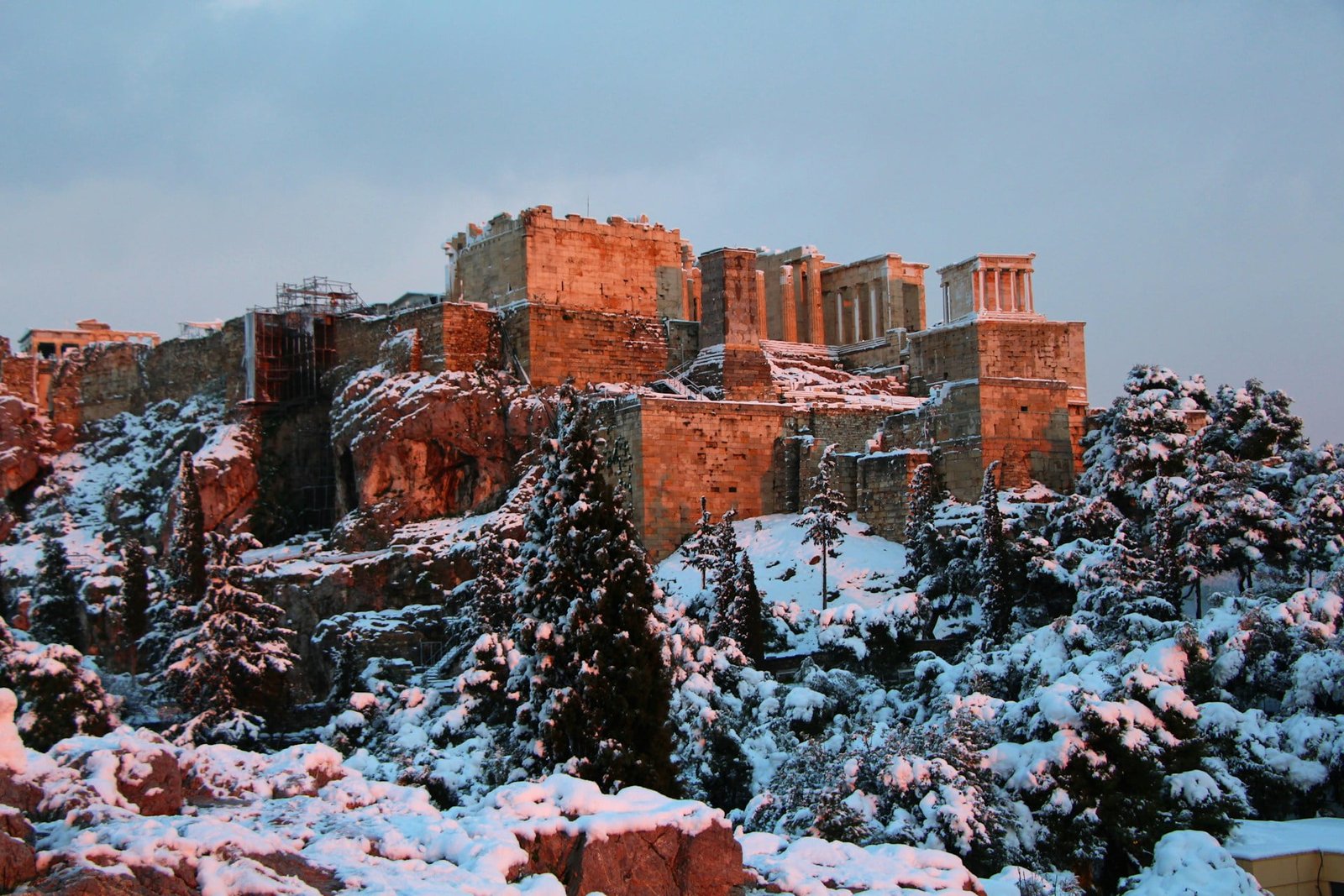 The Acropolis of Athens covered in snow under a dusky sky, an unusual sight indicating the worst time to visit Greece due to atypical weather conditions.