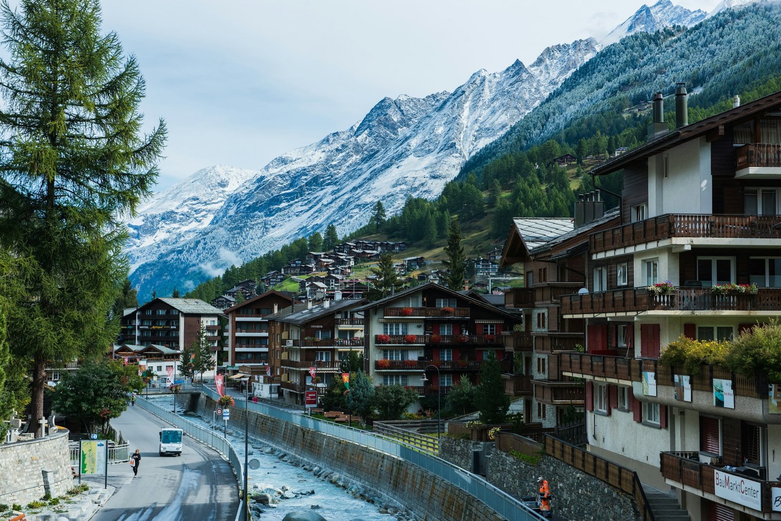 A picturesque Swiss village nestled in the foothills of snow-capped mountains, showcasing charming wooden chalets, winding roads, and a flowing river, encapsulating the serene beauty and allure of exploring Switzerland.