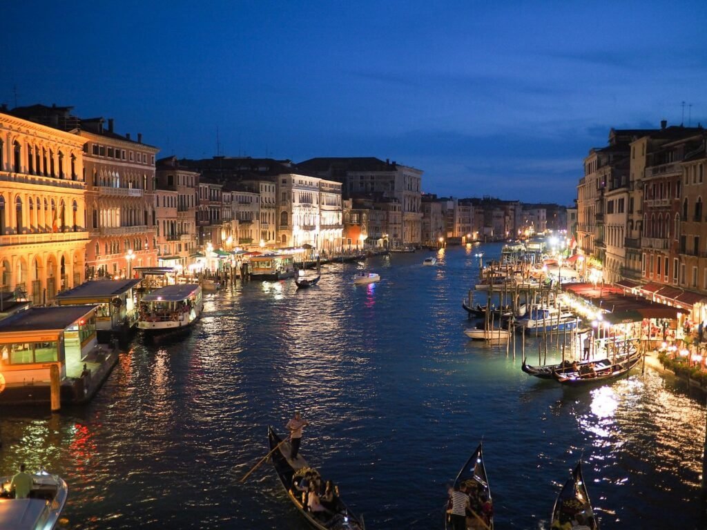 Evening view of a bustling canal in Venice with illuminated buildings and boats, perfect for a Multi-City Trip to Europe.