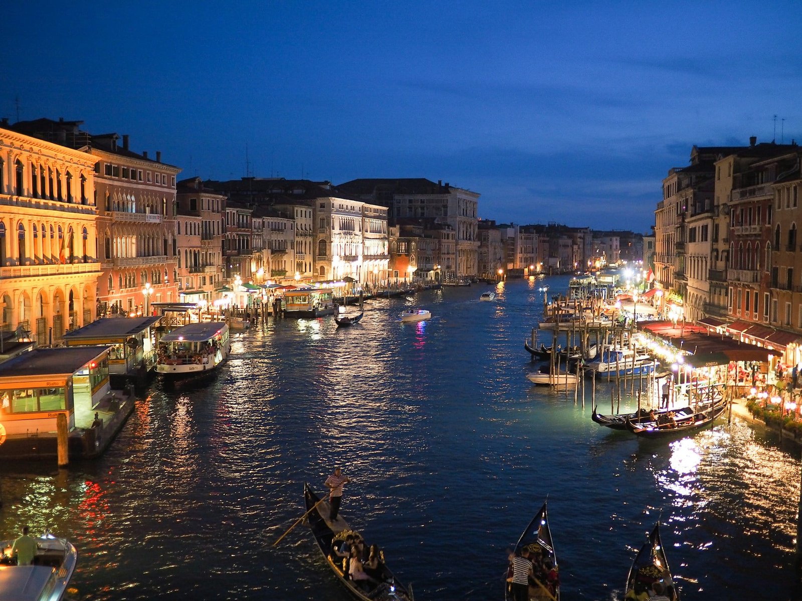 Evening view of a bustling canal in Venice with illuminated buildings and boats, perfect for a Multi-City Trip to Europe.