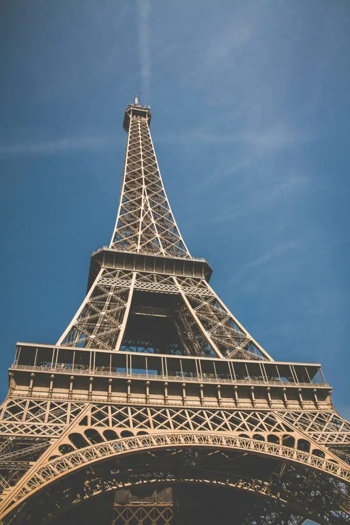 Upward view of the Eiffel Tower in Paris against a clear blue sky, showcasing the intricate iron lattice design and capturing the iconic architecture from a unique perspective.