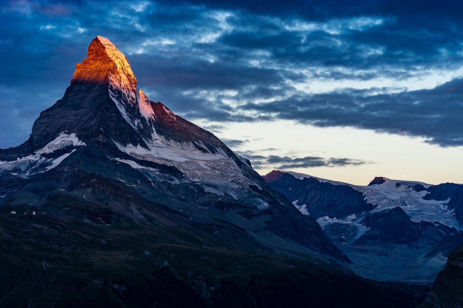 Majestic Matterhorn peak bathed in the warm glow of sunrise, with snow-covered slopes and rugged terrain, inviting travelers to plan a trip to Switzerland.