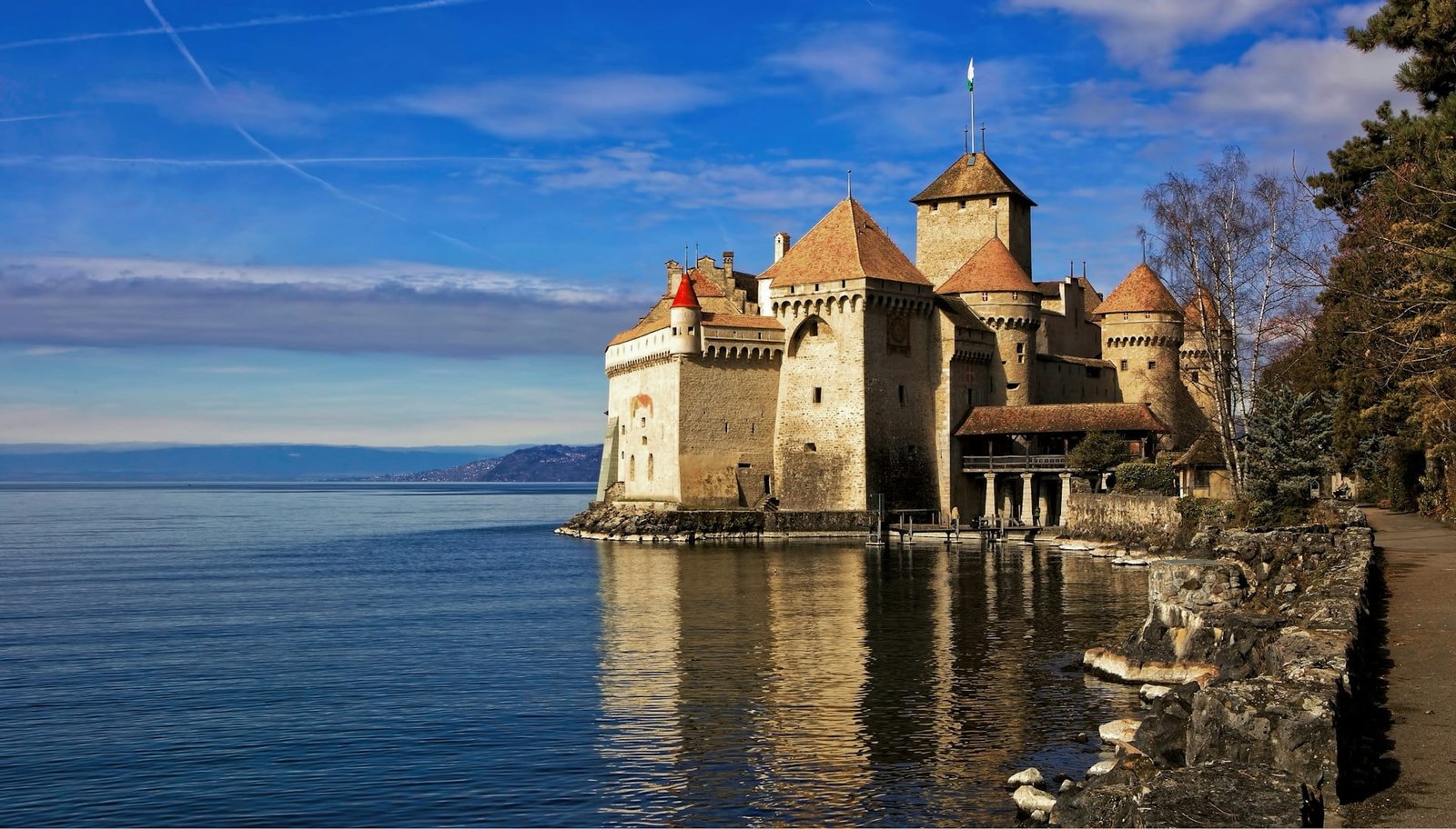 The Castle Veytaux, also known as Chillon Castle, standing majestically on the shores of Lake Geneva in Switzerland, with mountains faintly visible in the background under a clear blue sky – a must-see landmark when visiting Switzerland for the first time.