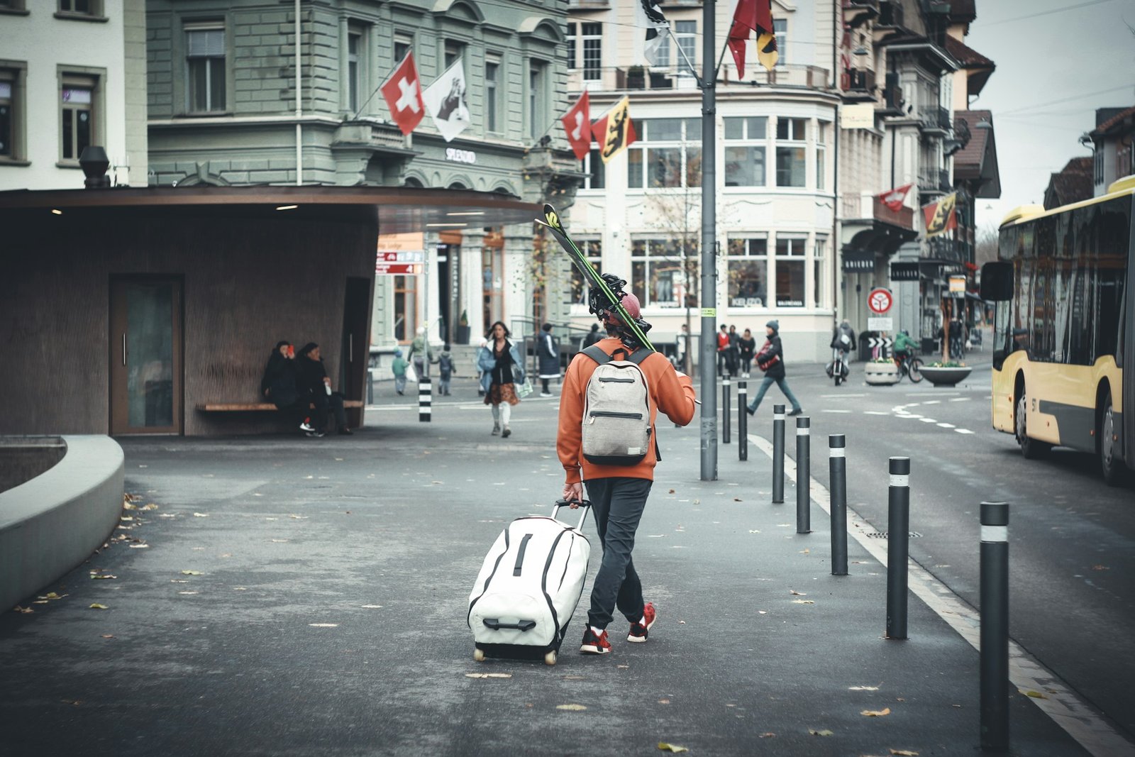 A lone traveler walks through a Swiss town, pulling a large bag and carrying skis on their shoulder – capturing one of the unique reasons to visit Switzerland in winter.