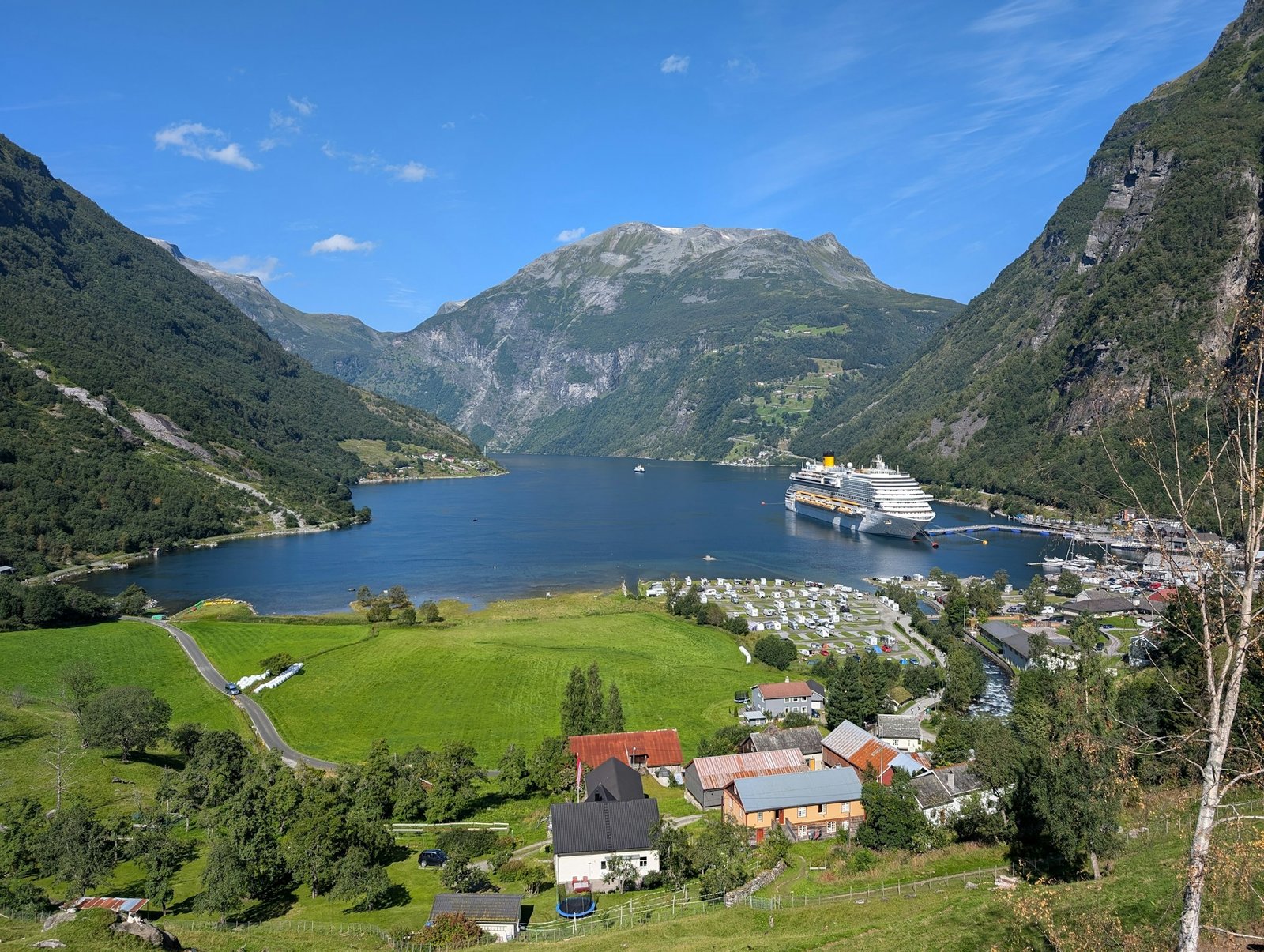 A scenic view of Geirangerfjord in Norway, featuring green hills, a cruise ship, and calm blue waters — is Norway worth visiting?