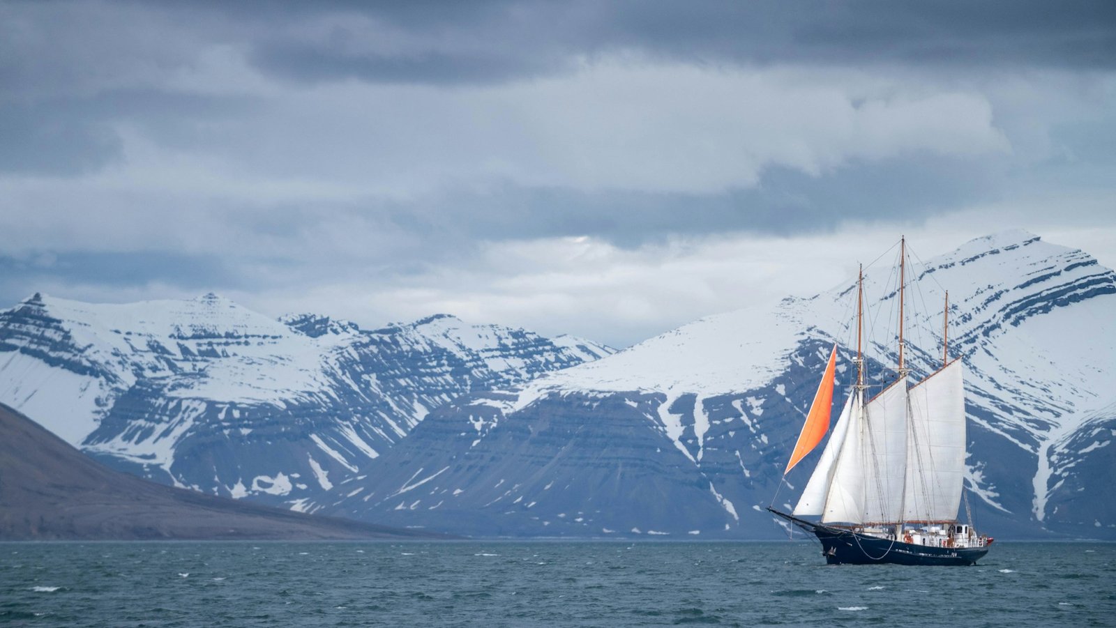 A ship with orange sails on icy waters with snowy mountains in Svalbard, taken during a trip to Norway.