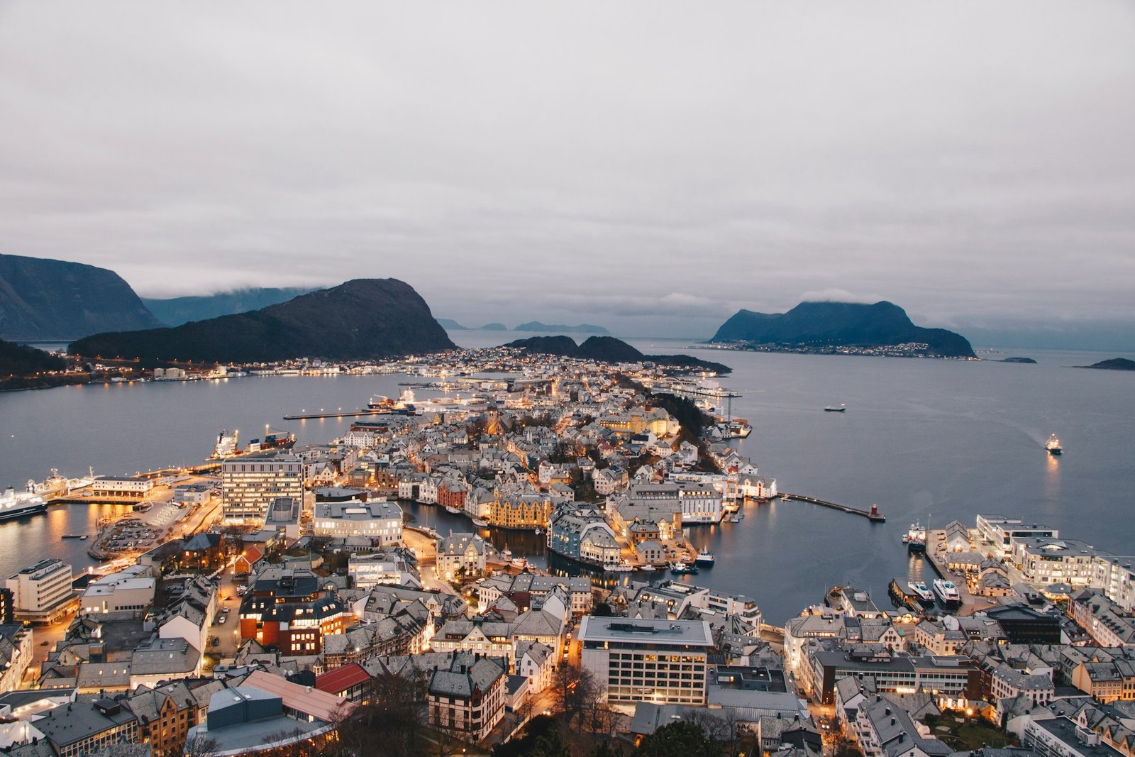 A panoramic view of Ålesund, the best city to visit in Norway, featuring its scenic harbour and illuminated buildings against a mountainous backdrop.