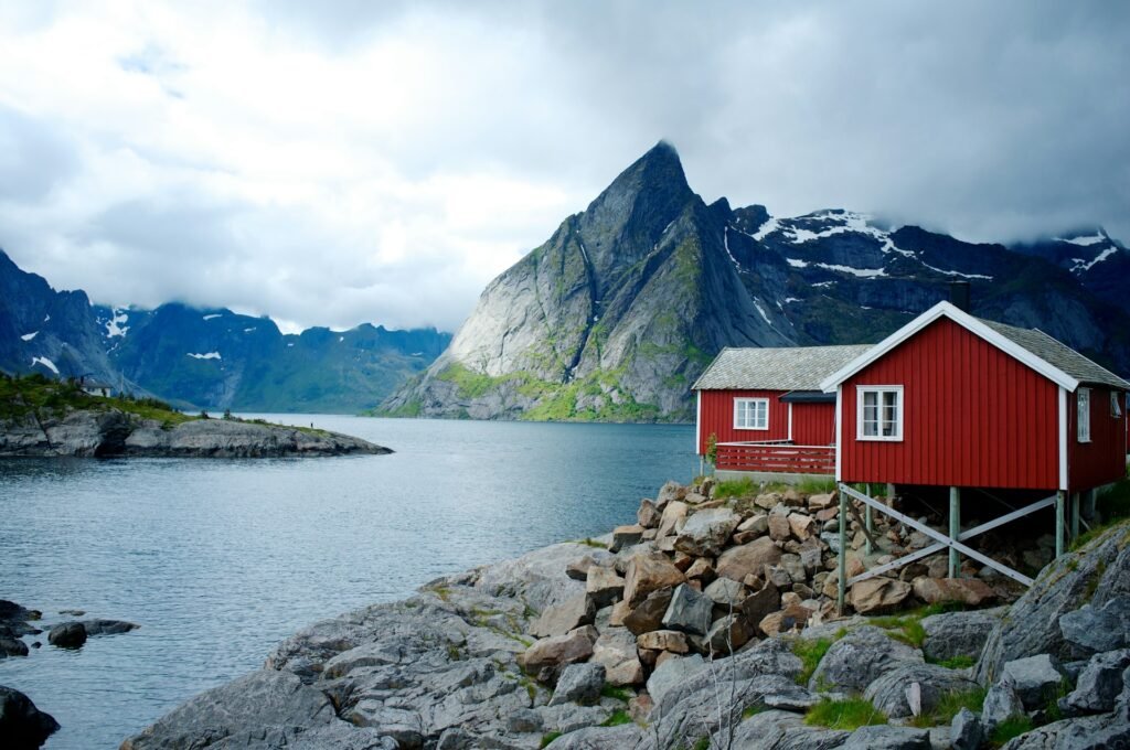 Is Norway a Good Place to Visit? Find Out Now! A red cabin on rocky shores by a fjord with dramatic mountains in the background. Is Norway a good place to visit?