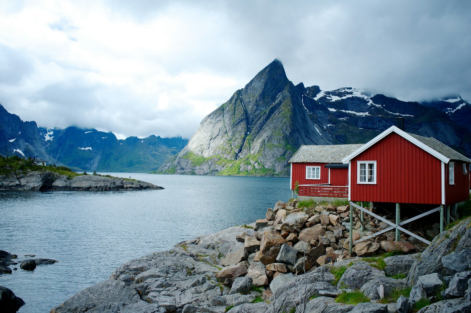 A red cabin on rocky shores by a fjord with dramatic mountains in the background. Is Norway a good place to visit?