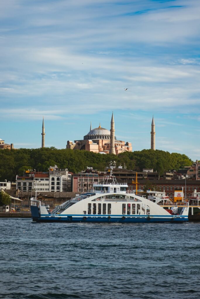 Destinations Scenic view of the Hagia Sophia in Istanbul with a ferry crossing the Bosphorus, capturing the city's iconic architecture and vibrant waterfront.