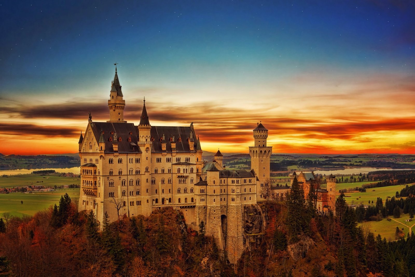 Aerial drone view of Neuschwanstein Castle in Bavaria, Germany, surrounded by lush forests and mountains.
