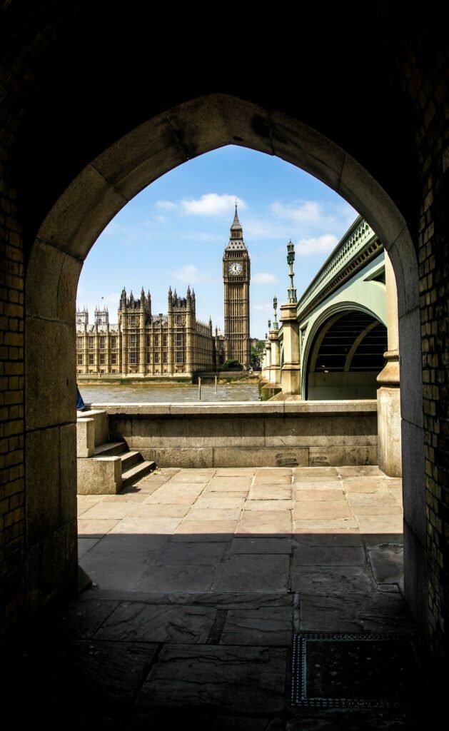 Destinations Big Ben and Houses of Parliament viewed from under an arch near Westminster Bridge, London. Iconic London landmark with a scenic Thames River backdrop.